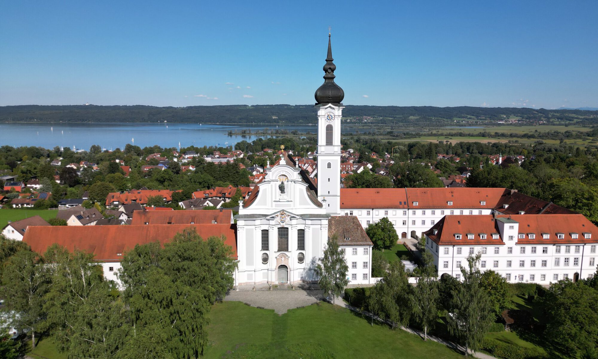 Luftaufnahme des Klosters Dießen mit barocker Stiftskirche, Zwiebelturm und dem Ammersee im Hintergrund